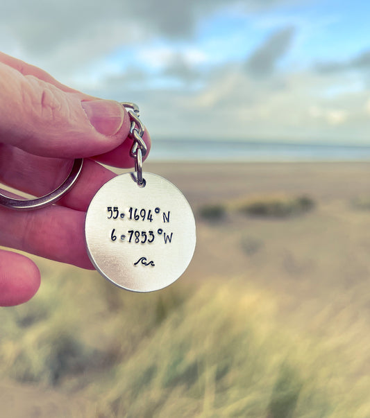 A silver coloured aluminium disc keyring, handstamped with co ordinates