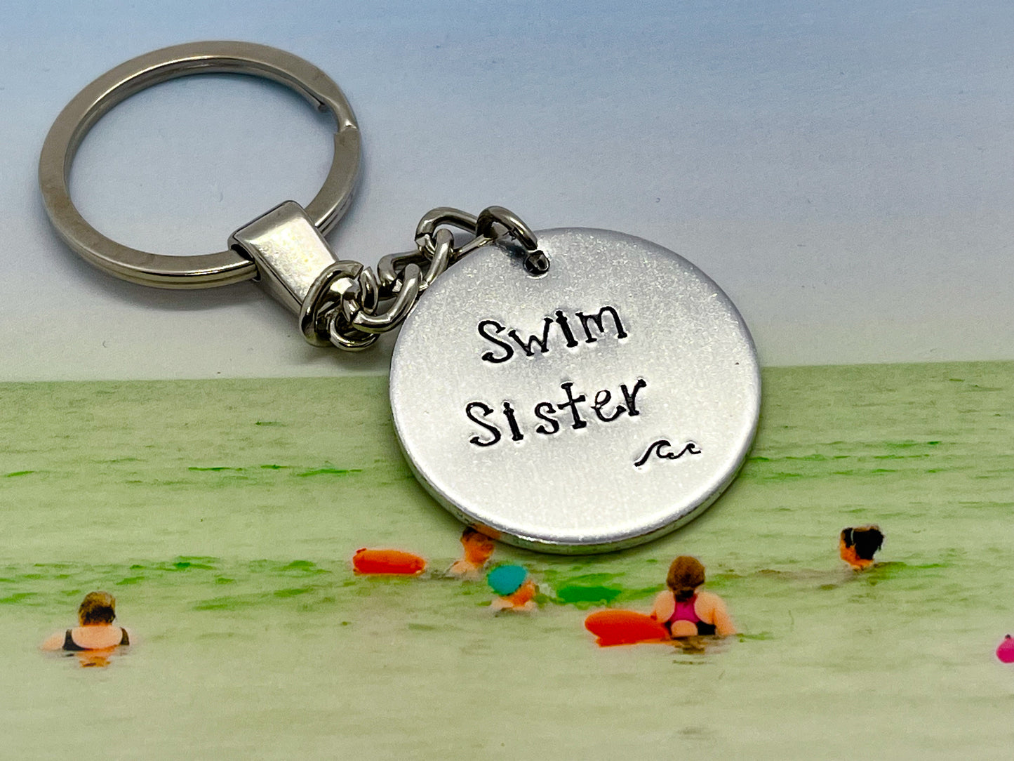 A silver coloured aluminium disc keyring, handstamped with the words Swim Sister