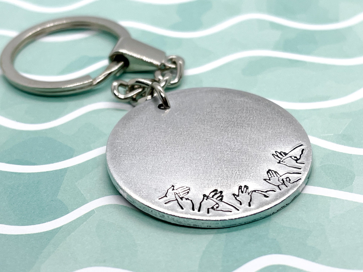 A silver coloured aluminium disc keyring, handstamped with British Sign Language symbols