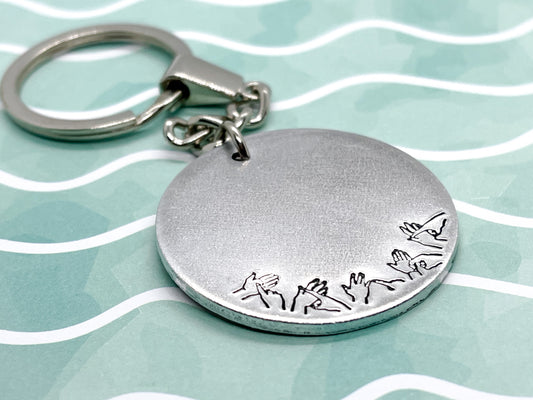 A silver coloured aluminium disc keyring, handstamped with British Sign Language symbols