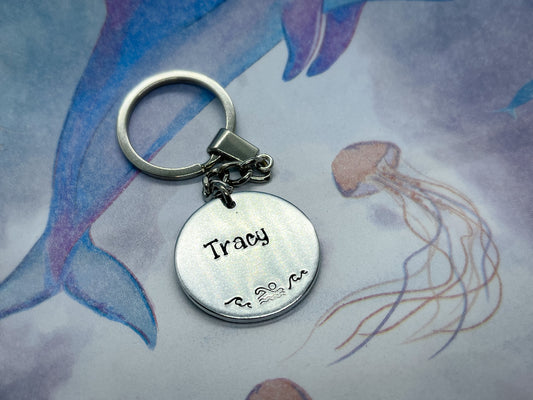 A silver coloured aluminium disc keyring, handstamped with a name and swimmer design