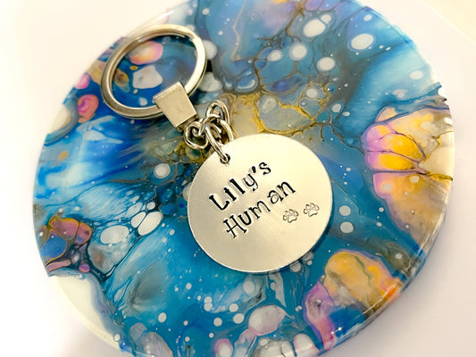 A silver coloured handstamped aluminium disc keyring with pawprints and the words Lily's Human